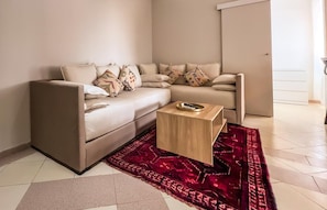 Ein modernes Wohnzimmer mit einem beigen Sofa, gemusterten Kissen, einem kleinen Holztisch und einem roten Teppich mit Muster.