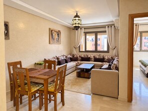 A living room with a sofa, a dining table with chairs, a coffee table, and a hanging light fixture. - Guéliz - Stylish Apartment with Balcony (Marrakesh)