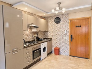 A modern kitchen with built-in appliances, a clock on the wall, and a wooden door. - Guéliz - Stylish Apartment with Balcony (Marrakesh)