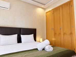 A hotel room with a bed, a wooden wardrobe, and a wall-mounted air conditioner. - Guéliz - Stylish Apartment with Balcony (Marrakesh)