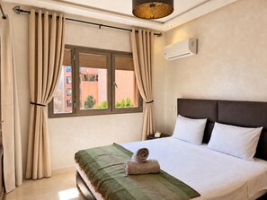 Quarto de hotel com cama, cortinas, aparelho de ar condicionado e janela com vista para edifícios.