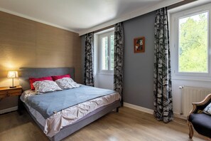 A bedroom with a bed, a nightstand, a lamp, a chair, a window, and curtains. - Exclusive Estate - La Chapelle aux Acacias (Caucalières)