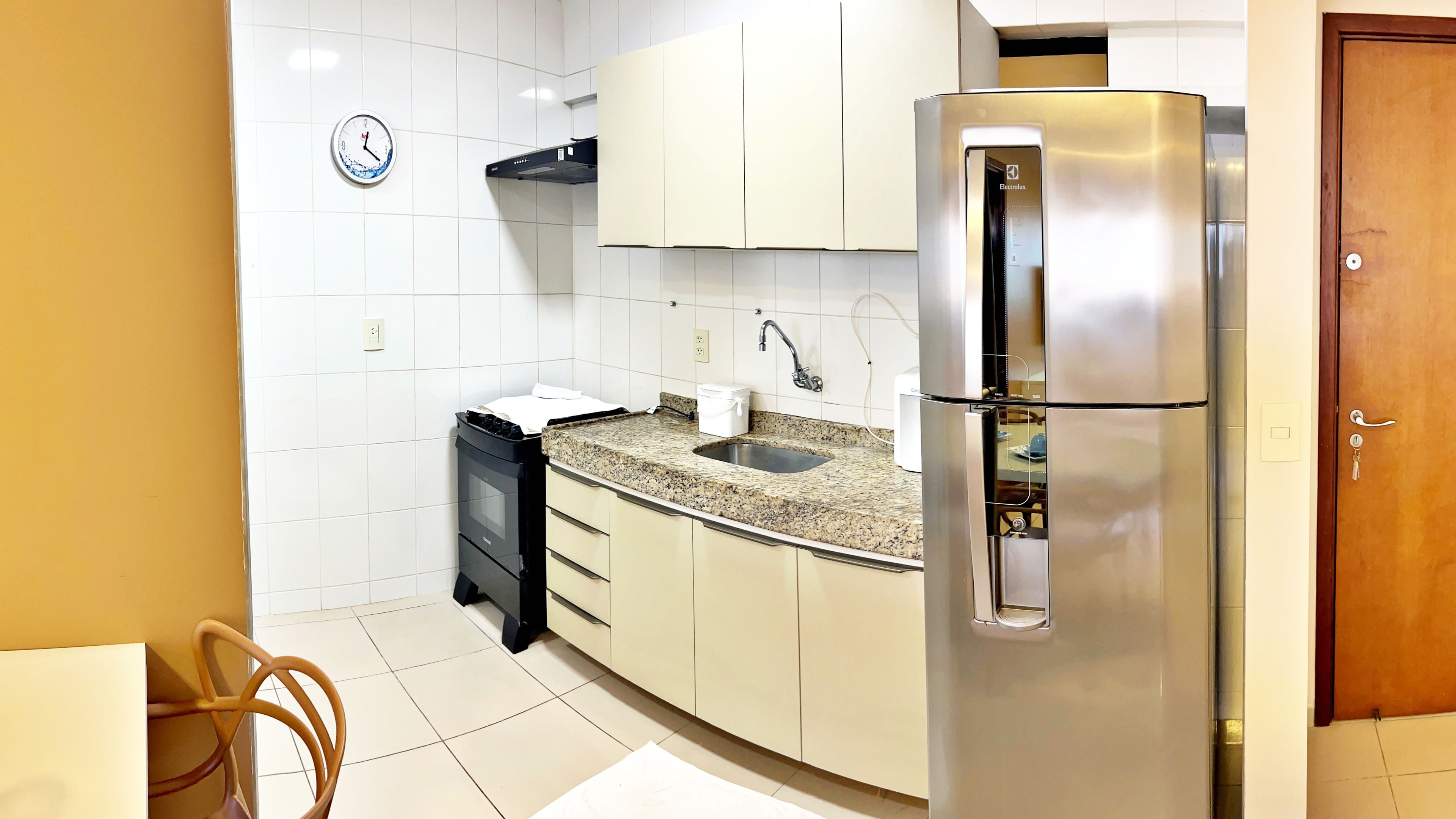 Una cocina con un refrigerador de acero inoxidable, un lavamanos y un reloj en la pared.