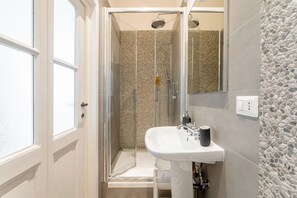 Un baño con cabina de ducha de vidrio, un lavabo blanco y una pared con textura de piedra.