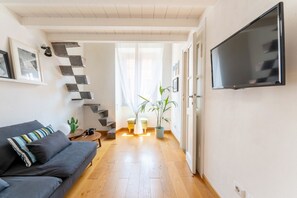Ein modernes Wohnzimmer mit einer Couch, einem flachbildfernseher an der Wand, einer Treppe mit Rautenmuster und einem Topfpflanzen.