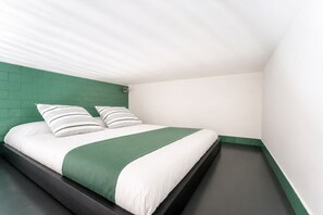 Ein Einzelbett mit einer grün-weißen Tagesdecke, zwei Kissen und einem dunklen Kopfteil in einem Eckzimmer mit weißen Wänden und einer grünen Akzentwand.