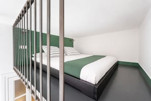 Una cama individual con una colcha verde y blanca en una habitación con paredes verdes y suelo oscuro.