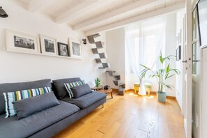 Una sala de estar moderna con un sofá gris, suelo de madera y una escalera que sube a otro nivel.