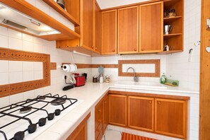 A kitchen with wooden cabinets, a gas stove, a sink, and a tiled backsplash. - Roma Family Terrace, Spacious Apt in San Giovanni (Rome)