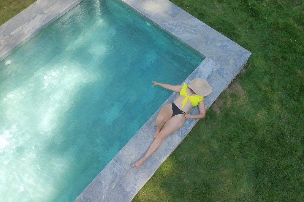 A person lying on a poolside with a clear view of the pool and surrounding grass.