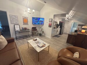 A modern living room with a flat-screen TV, a coffee bar, and a kitchen area.
