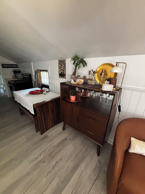 A cozy room with a bed, a wooden dresser, a coffee bar, and a dining area.