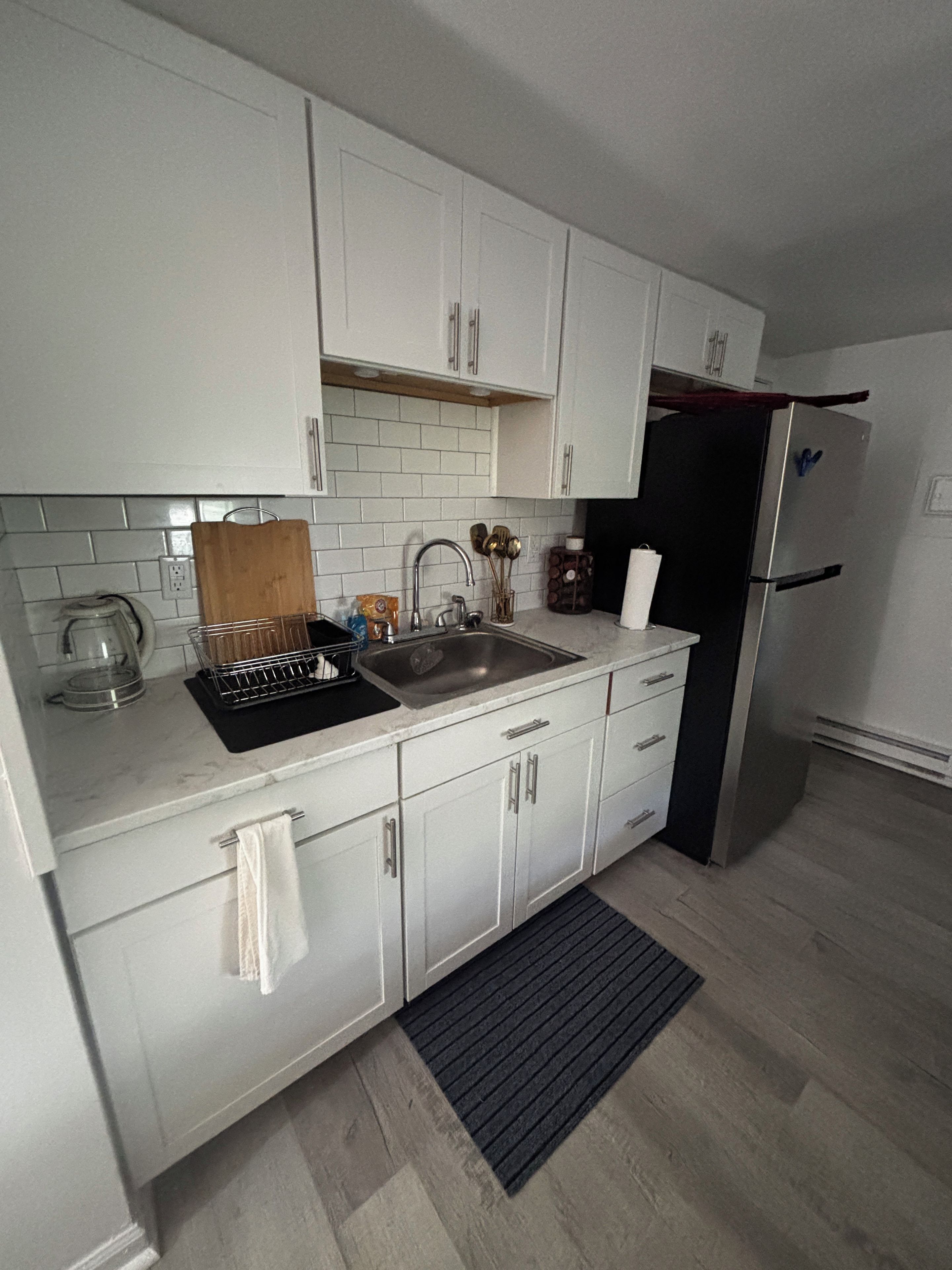 Una cocina moderna con armarios blancos, un lavamanos de acero inoxidable y un refrigerador negro.