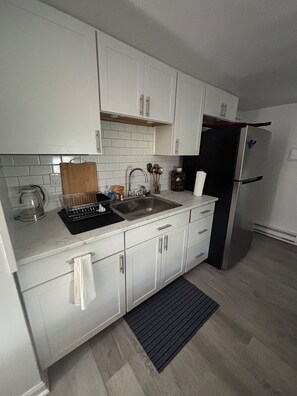 A modern kitchen with white cabinets, a stainless steel sink, and a black refrigerator.