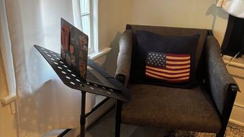 Una habitación con un sillón gris, un escritorio negro con una computadora portátil y una alfombra estampada.