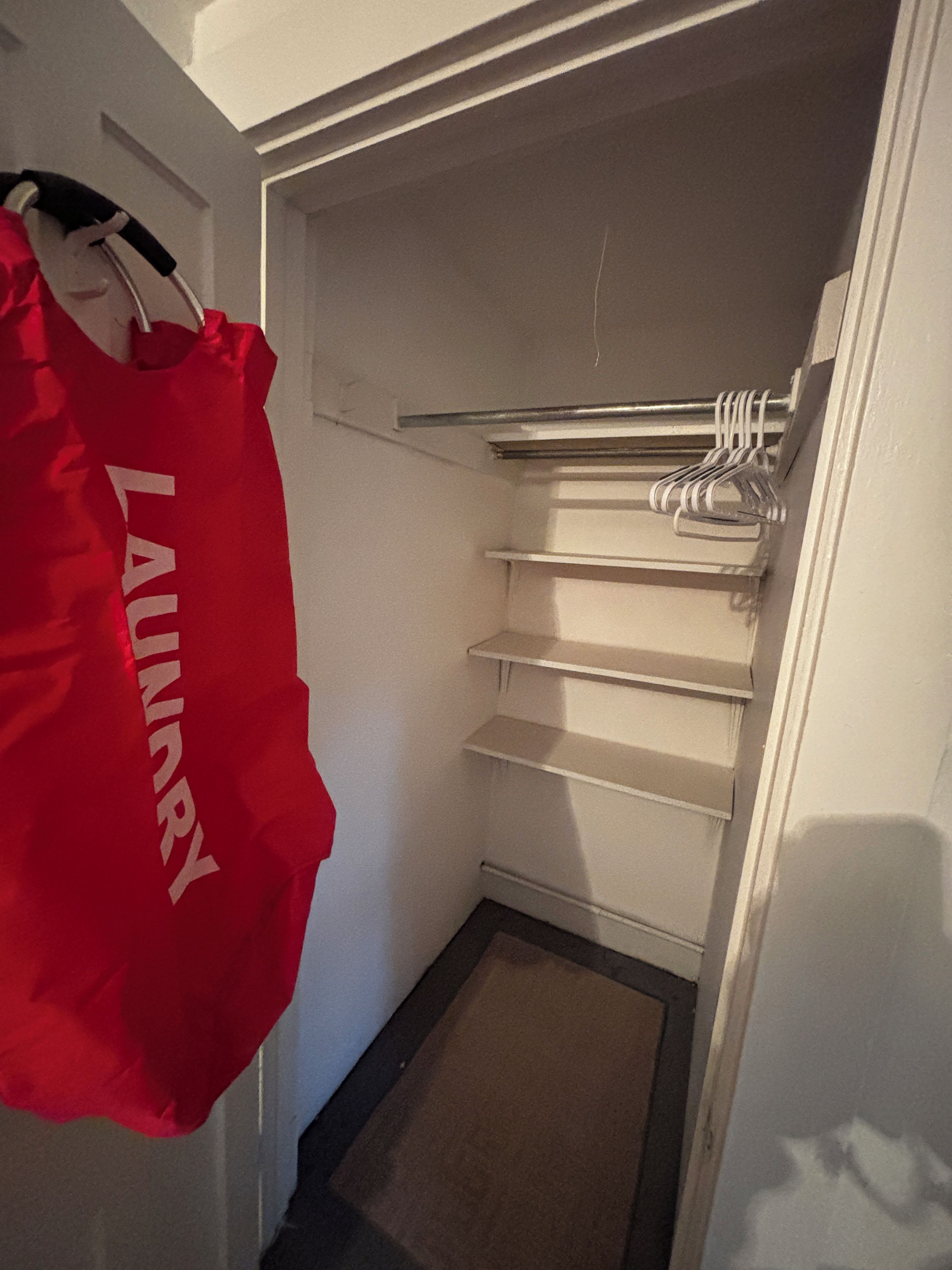 A laundry area with a red bag hanging on a hook and a metal rack with hangers.