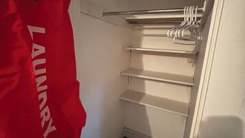 A laundry area with a red bag hanging on a hook and a metal rack with hangers.