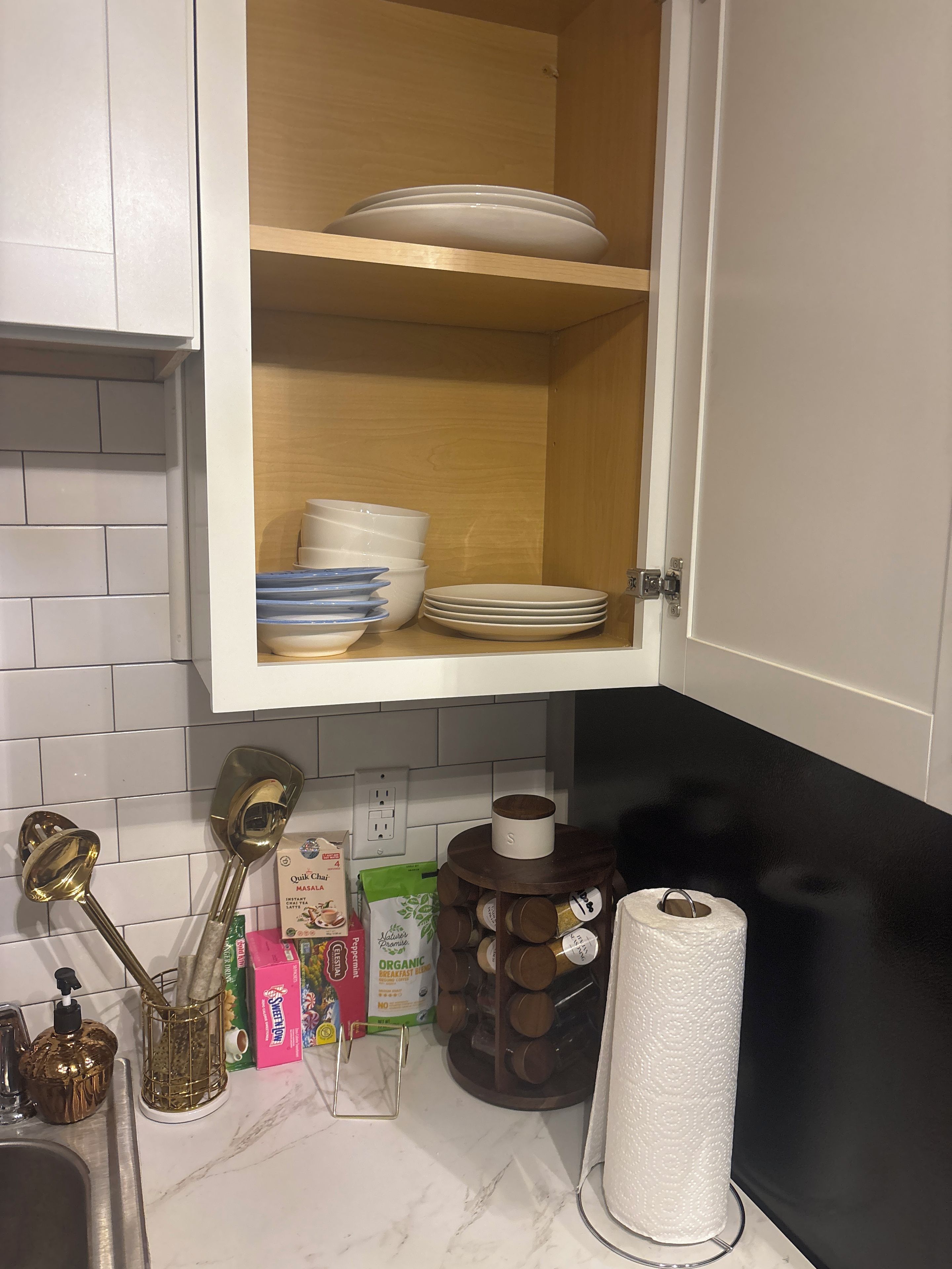 A kitchen with white cabinets, a marble countertop, and a wooden shelf above holding plates and bowls.