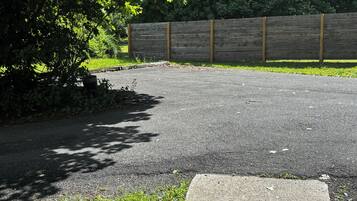 A paved driveway leading to a wooden fence, surrounded by greenery and a concrete path.