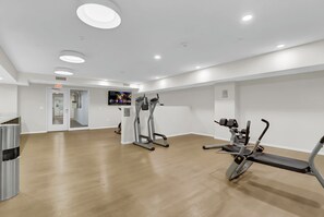 Un gimnasio moderno con equipo de ejercicio, un televisor y un bote de basura.