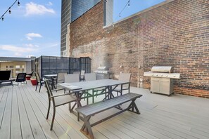 An outdoor patio with a wooden deck, a table with chairs, a grill, and a brick wall. - PremiumStays: Cozy, Modern, 1 bed loft - Downtown - Playhouse Square (Cleveland)