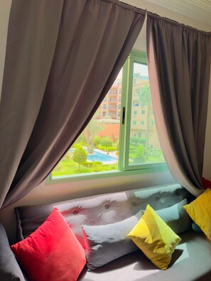 Ein Fenster mit Vorhängen, Blick auf ein Gebäude und ein Bett mit Kissen.