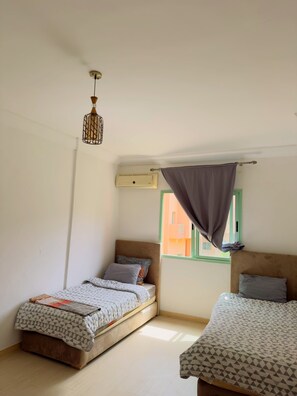 Ein Schlafzimmer mit zwei Betten, einer Pendelleuchte, einer Klimaanlage und einem Fenster mit Vorhang.