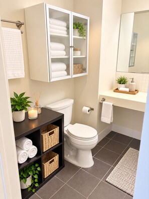 Ein modernes Badezimmer mit Toilette, einem Schrank mit Handtüchern, einem Spiegel und einem Regal mit Pflanzen und Körben.