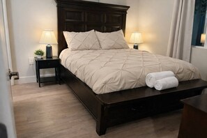 Ein ordentlich bezogenes Bett mit Kopfteil, zwei Nachttischen mit Lampen und einem zusammengerollten Handtuch auf dem Bett.