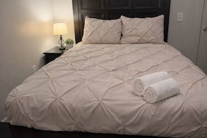 Una cama bien hecha con cubrecolcha acolchado y dos toallas enrolladas a un lado.
