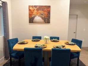 Un comedor con mesa de madera, sillas azules y un cuadro de un puente en tonos otoñales en la pared.