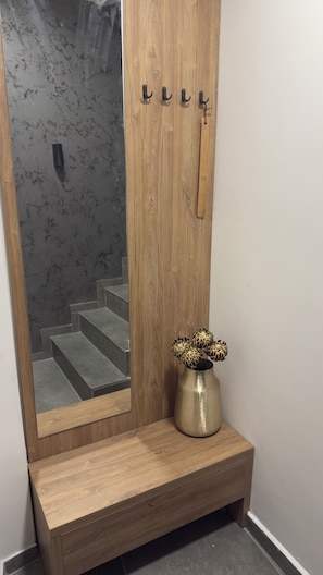 Un banco de madera con un jarrón de flores, un espejo y una puerta con manija.