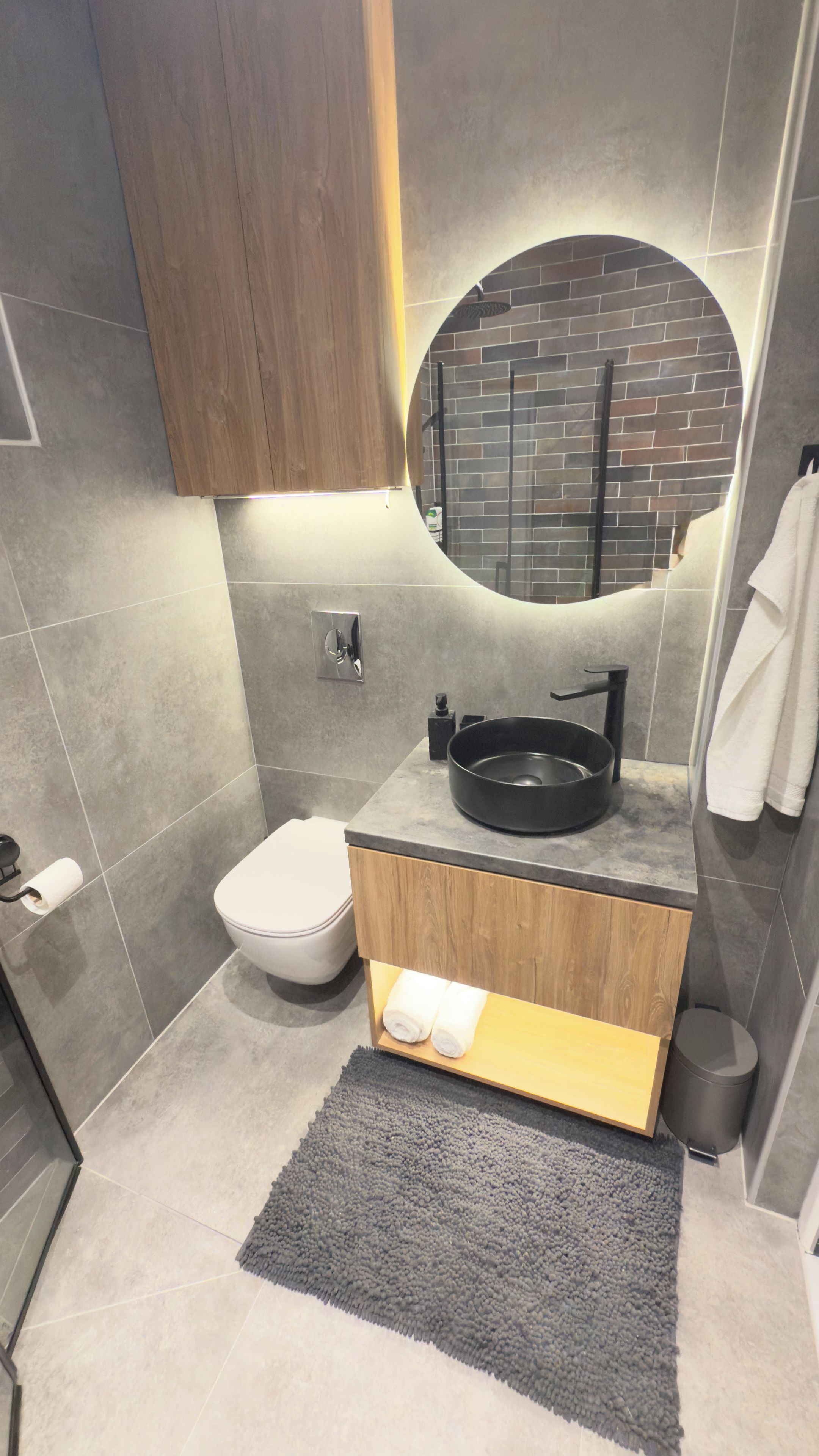 A modern bathroom with a round mirror, a black sink, and a toilet.
