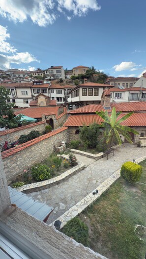 A courtyard with stone pathways, potted plants, and traditional buildings with red-tiled roofs.