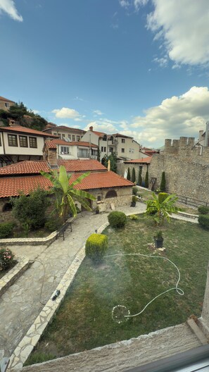 A courtyard with stone pathways, a grassy area, and traditional buildings with red-tiled roofs.