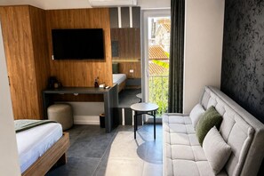 A modern hotel room with a bed, a desk, a sofa, and a TV.