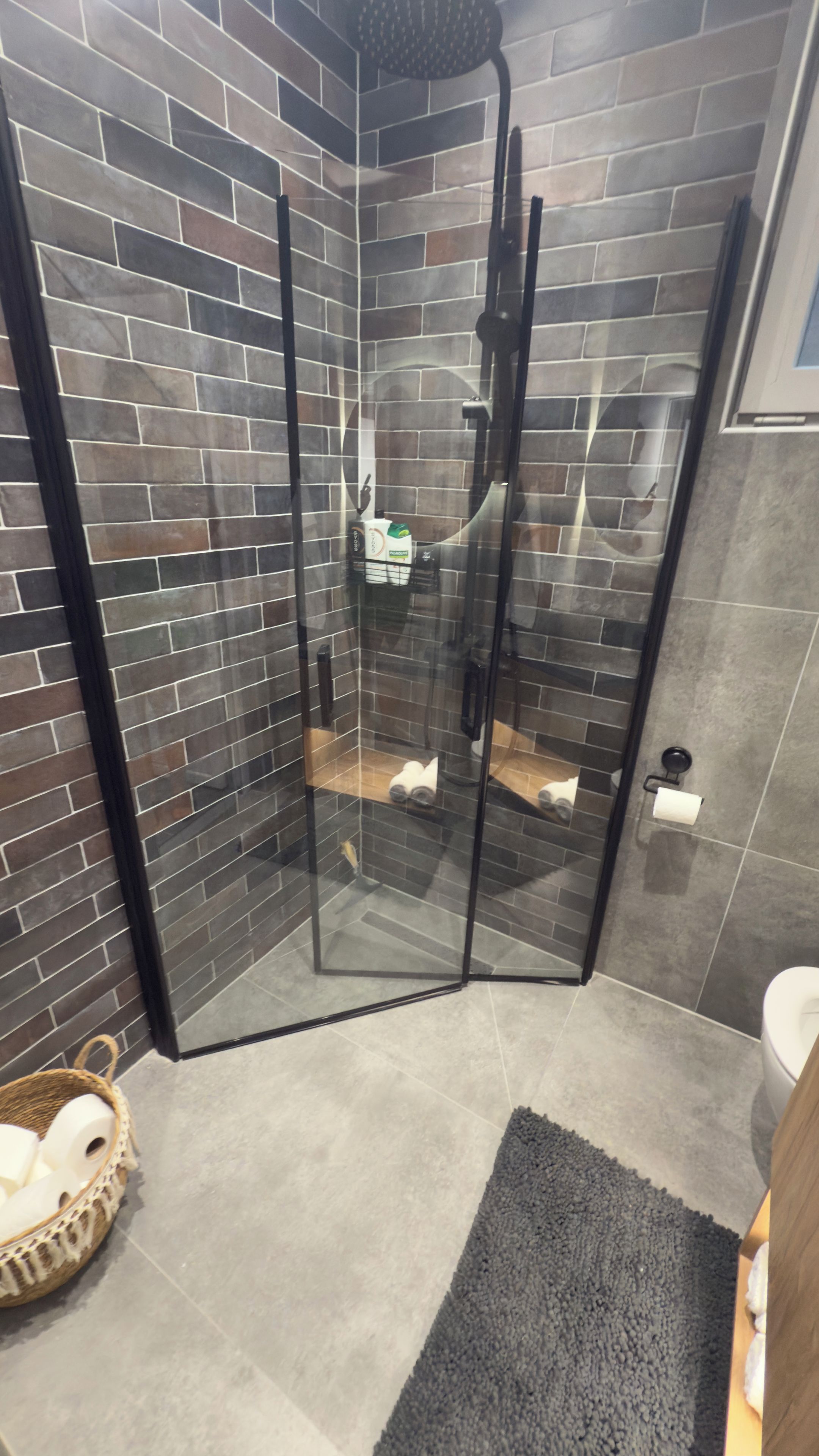 A shower with glass doors, a tiled wall, a toilet, and a rug.