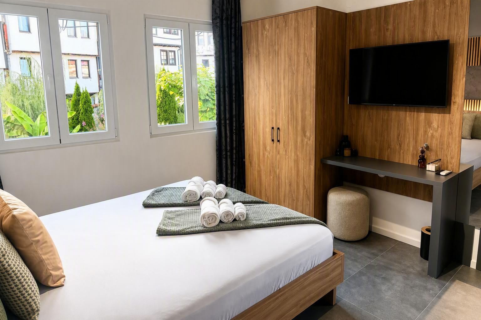 Un dormitorio moderno con cama, televisor de pantalla plana, armario de madera y vista a zonas verdes.