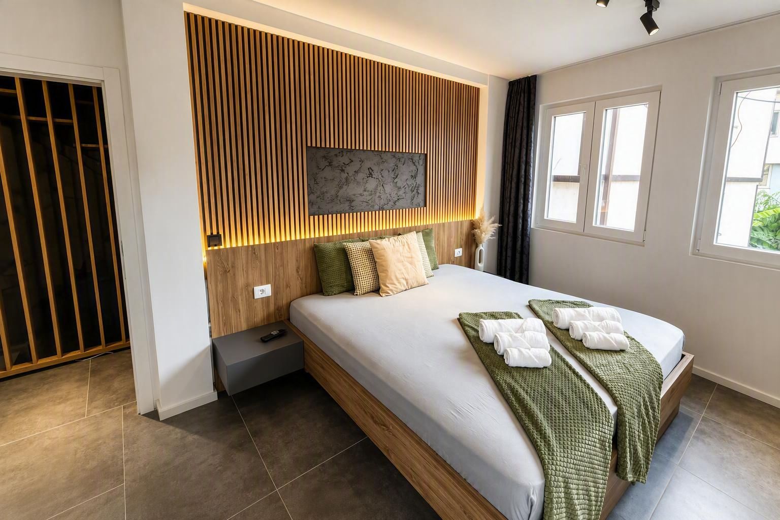 A modern bedroom with a large bed, a wooden headboard, a flat-screen TV, and a window with curtains.