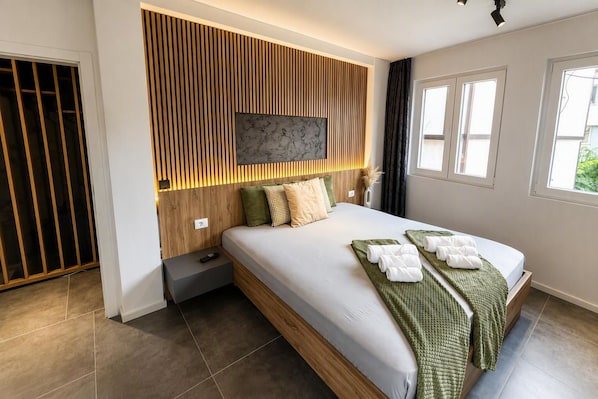 Un dormitorio moderno con una cama grande, cabecera de madera, televisor de pantalla plana y ventana con cortinas.