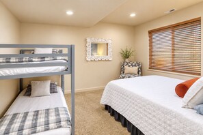 A bedroom with bunk beds, a single bed, a mirror, a chair, and a window with blinds.