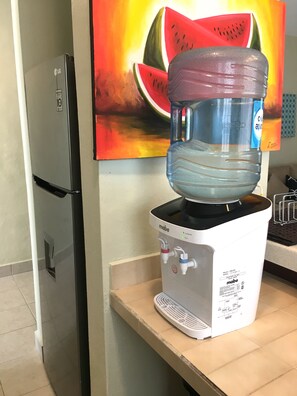 A water dispenser with a water jug on top, a refrigerator, and a painting of a watermelon on the wall. - Casa Christi - Private Pool, 2 BR, Sleeps 6 - Townhouse on the Right Side (Cozumel)