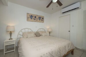 A bedroom with a bed, two bedside tables, a ceiling fan, an air conditioning unit, and a door. - Casa Christi - Private Pool, 2 BR, Sleeps 6 - Townhouse on the Right Side (Cozumel)
