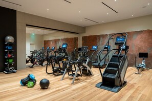 Un gimnasio moderno con varias cintas de correr, equipo de levantamiento de pesas y suelo de madera.