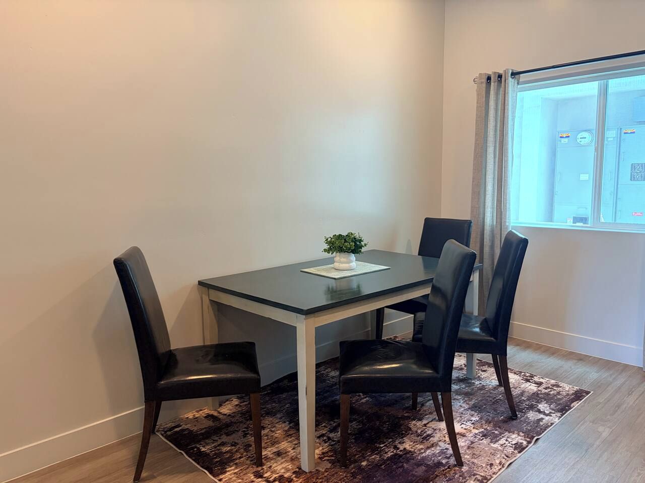 A dining area with a table and four chairs, a small plant on the table, and a window with curtains.
