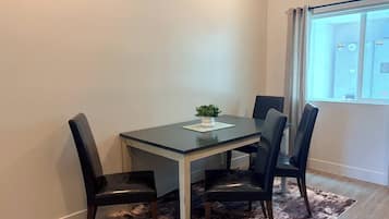 A dining area with a table and four chairs, a small plant on the table, and a window with curtains.