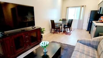 A living room with a TV, a dining area with chairs, a sofa, and a kitchen area with a fridge.