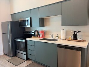 Una cucina moderna con mobili grigi, un frigorifero in acciaio inossidabile, un forno a microonde, un forno, una lavastoviglie e un lavello.
