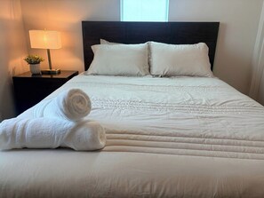 A neatly made bed with a white duvet and pillows, a rolled white towel, a bedside lamp, and a small potted plant on a nightstand. - Luxury 1BR Retreat | Pool, Gym & Gated Community (Mesa)
