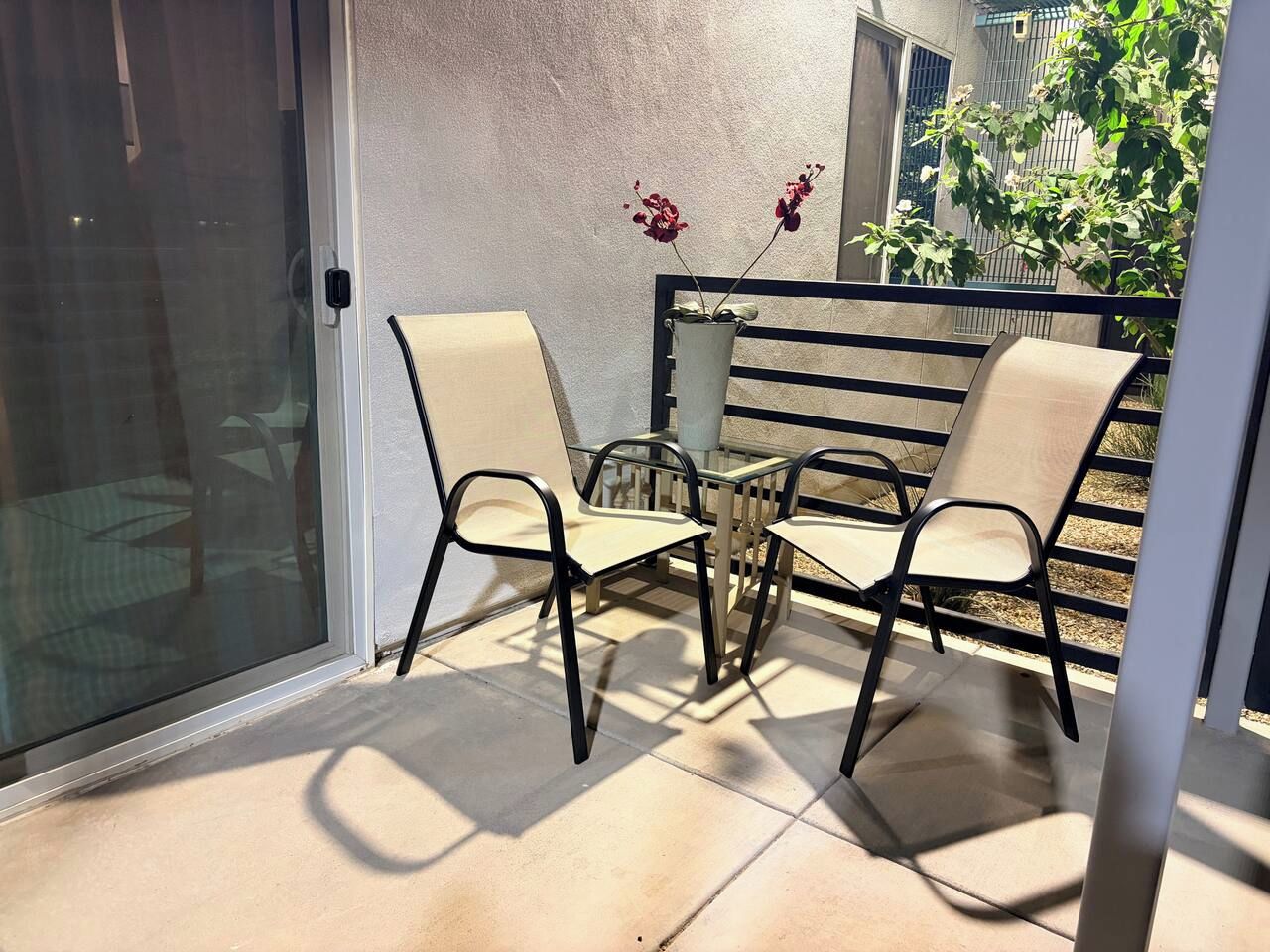 Une terrasse avec deux chaises et une table, une porte vitrée et une plante en pot.